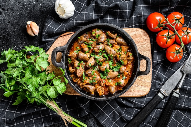 Фото Запеченная куриная печень сердца в чугунной сковороде. черный фон. вид сверху