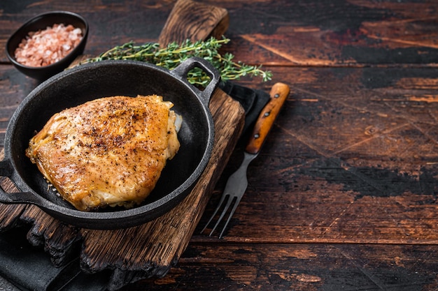 Baked chicken thigh in a pan with rosemary and salt. Dark wooden background. Top View. Copy space.