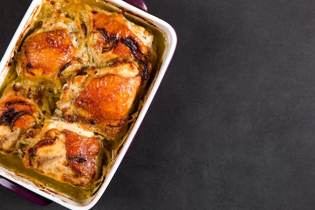 Baked chicken thighs with onions in ceramic form on a stone table, copy space.