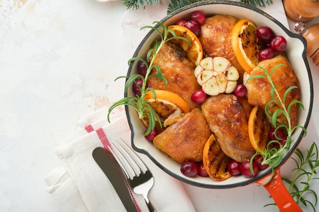 Photo baked chicken thighs with orange cranberry and spicy herbs rosemary servered in frying pan on light background festive christmas dinner concept menu top view copy space