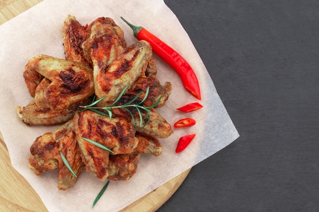 Photo baked chicken wings with and sweet chili sauce on  wooden board over dark surface with copy space.