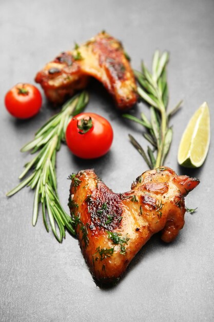 Baked chicken wings with tomatoes and rosemary on grey background