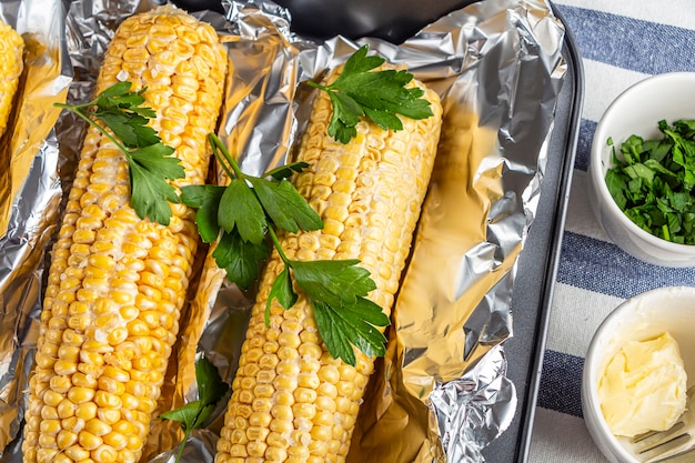 Baked corn with salt, butter and cilantro or parsley in foil on kitchen table