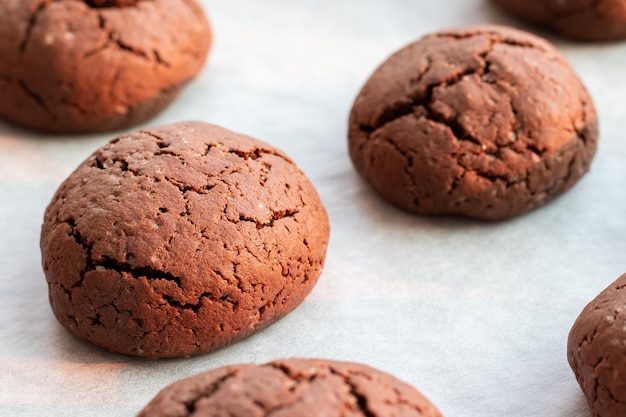 Baked cracked round chocolate cookies on baking sheet with parchment paper