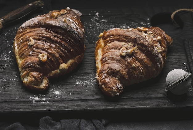 ボードに焼きたてのクロワッサンと粉砂糖の黒いテーブルを振りかけた朝食用の食欲をそそるペストリーx9