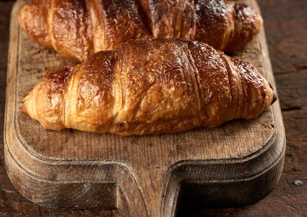 Baked croissants on brown kitchen board, black background