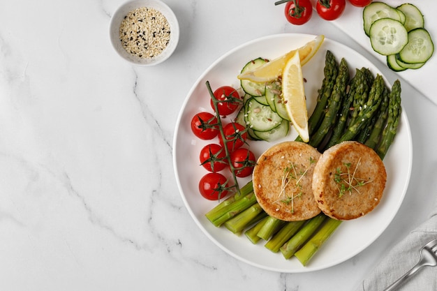 Baked cutlets with vegetables asparagus cucumbers and tomatoes cherry on white plate Diet dinner