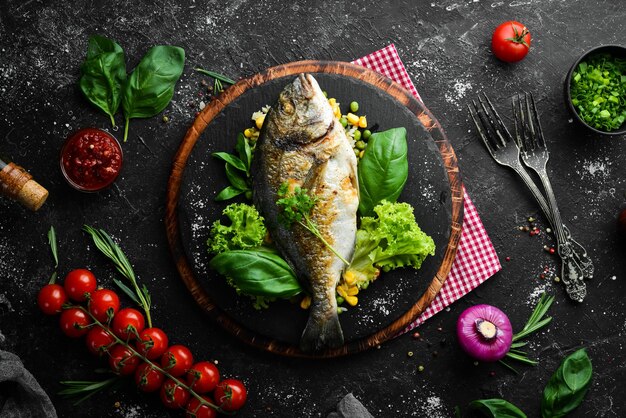 Pesce dorado al forno con riso e verdure su un piatto nero vista dall'alto spazio libero per il testo