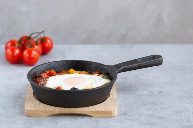 Foto uovo al forno con pomodori peperoni e spinaci in padella su fondo grigio ottimo per la colazione