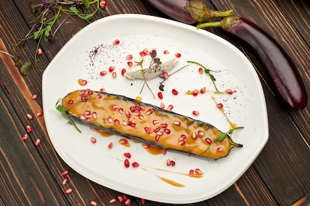 Baked eggplant with cheese and pomegranate seeds, on a white plate, on wooden table