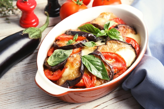 Baked eggplant with tomatoes cheese and basil in dishware on table closeup