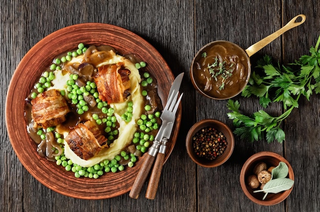 Baked faggots served with creamy mashed potatoes green peas and\
rich thick onion gravy on a clay plate british cuisine flat\
lay