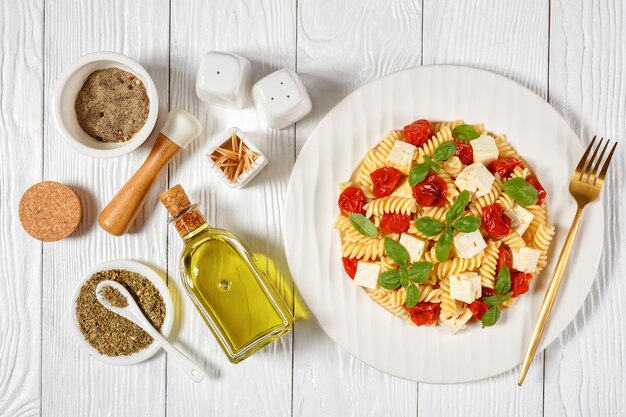 Baked feta cheese fusilli pasta with cherry tomatoes and basil on a white plate on a wooden table, flat lay, italian cuisine