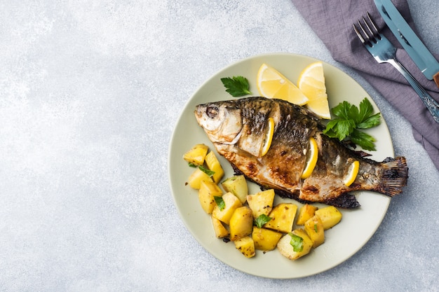 Baked fish carp with lemon greens and potatoes on a plate. Copy space