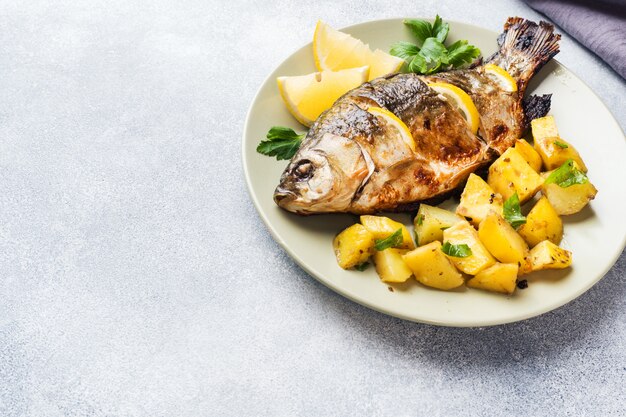 Baked fish carp with lemon greens and potatoes on a plate. Copy space