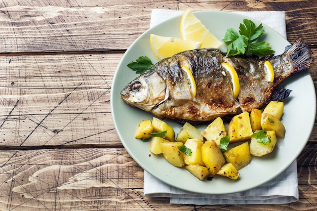 Carpa al forno del pesce con le verdure e le patate di limone su un piatto. di legno. copyspace