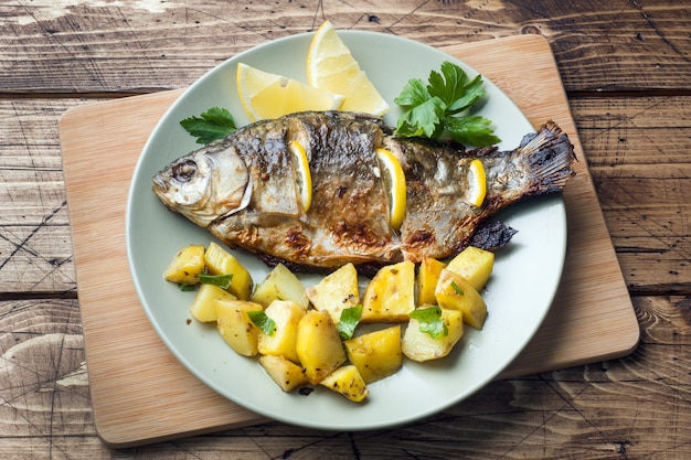 Baked fish carp with lemon greens and potatoes on a plate. Wooden .