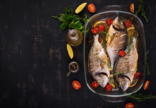 Baked fish dorado with lemon and herbs in baking pan on dark rustic background. Top view. Healthy dinner with fish concept. Dieting and clean eating