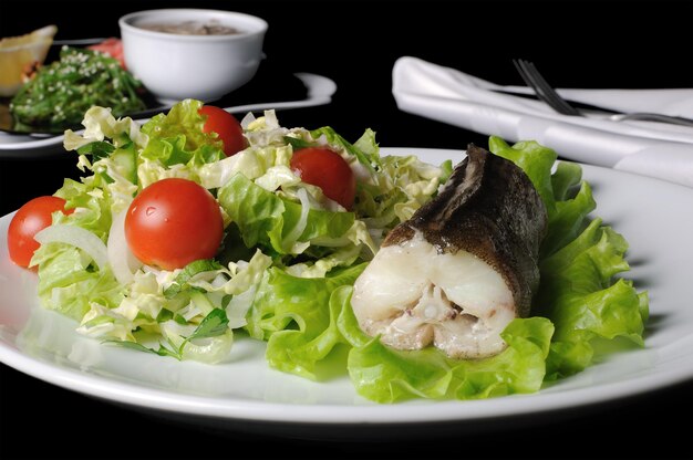 Photo baked fish king clip with a salad of green vegetables and cherry tomatoes