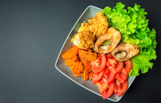 Baked fish with vegetables on a dark background