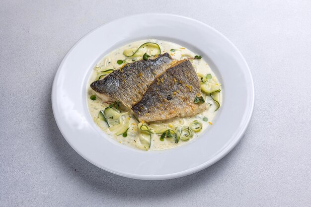 Foto pesce al forno con zucchine e aneto su un piatto bianco