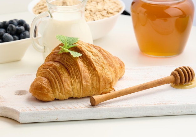 Baked fresh croissant on a wooden board milk and honey on a white table morning breakfast