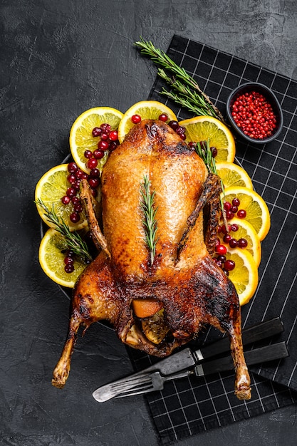 Baked goose stuffed with oranges and rosmarina. Festive table. Black background. Top view.