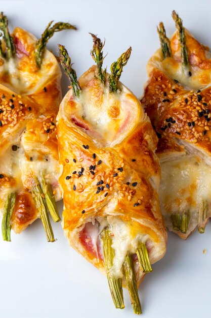 Photo baked green asparagus with ham and cheese in puff pastry sprinkled with sesame seeds and green basil leaves