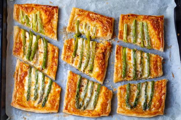 Photo baked green asparagus with ham and cheese in puff pastry sprinkled with sesame seeds and green basil leaves