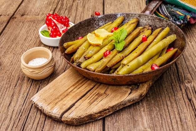 Baked green bean in pan with sesame seeds, pomegranate, mint and lemon