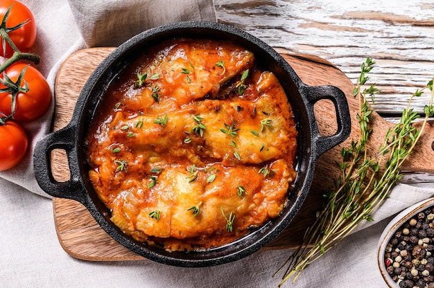 Baked halibut fish in a pan with tomato sauce