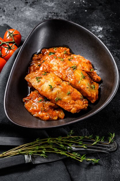 Baked halibut fish with tomato sauce. Black background. Top view