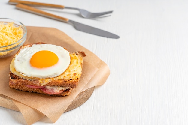 Baked hot French croque madame sandwich with ham and cheese topped with fried egg served on paper