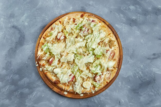 Baked italian pizza with cherry tomatoes, lettuce, parmesan, croutons, chicken on a wooden tray on a gray background. caesar pizza