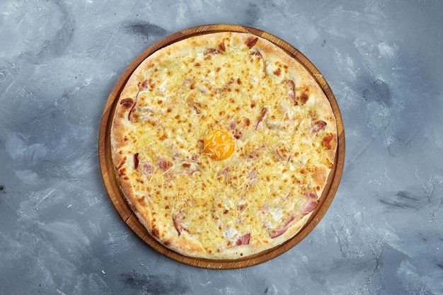 Baked Italian pizza with yolk, parmesan cheese, bacon and creamy sauce on a wooden tray on a gray background. Pizza carbonara