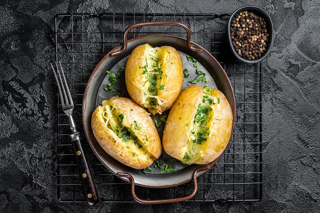 Baked jacket potatoes with cheese herbs and butter black\
background top view