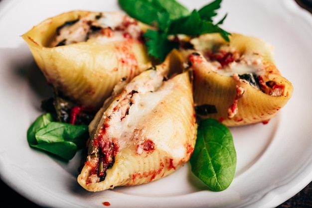 Pasta jumbo al forno ripiena di spinaci di manzo macinata e formaggio su piatto bianco