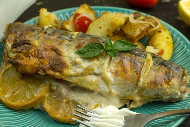 Baked mackerel carcass with lemon and vegetables on a plate.