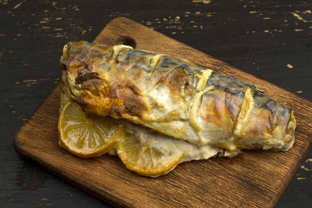 Baked mackerel carcass with lemon and vegetables on wooden board