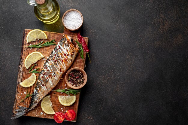 baked mackerel on a cutting board with lemon and spices on a stone background 