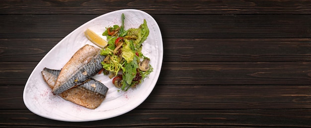 Baked mackerel fillet with salad and mushrooms on a plate on a wooden background