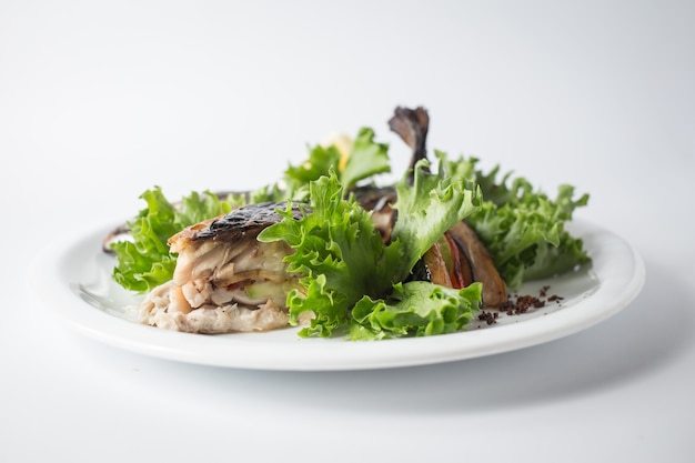 Baked mackerel with green salad and lemon on white plate.