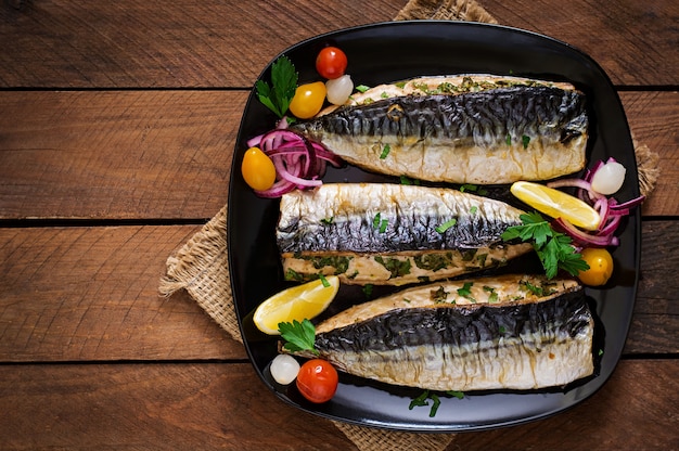 Baked mackerel with herbs and garnished with lemon and pickled vegetables. Top view