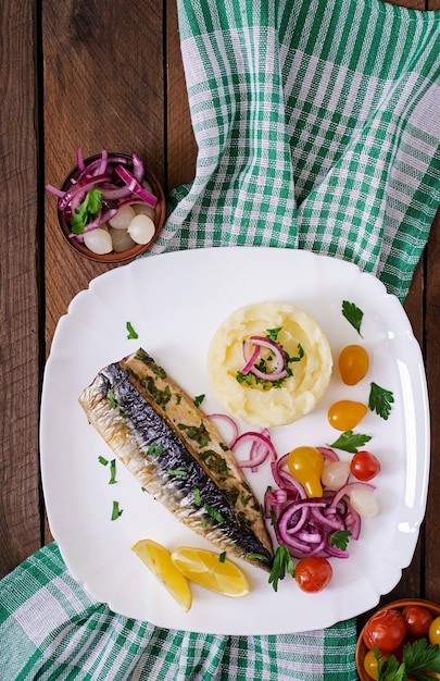 Baked mackerel with herbs and garnished with mashed potatoes and pickled vegetables. Top view