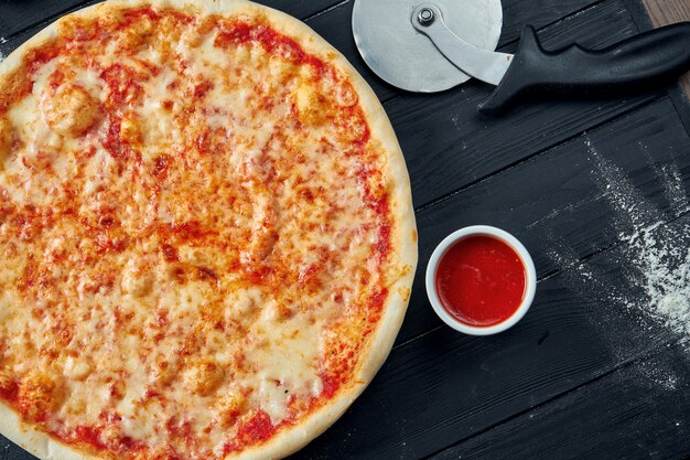 Baked margarita pizza with tomatoes and melted cheese, red sauce and on a black wooden table in a composition with ingredients. Top view