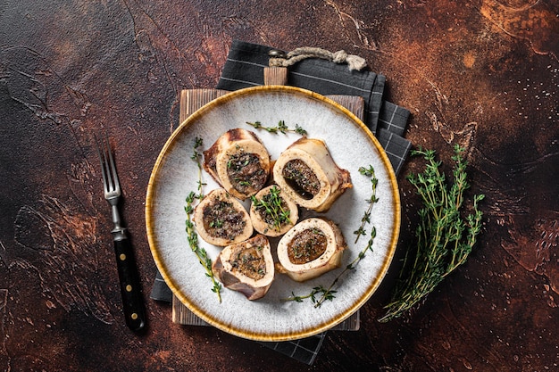 Baked marrow veal beef bones in plate with thyme and herbs. Dark background. Top view.