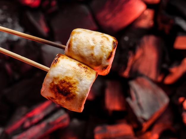 Baked marshmallows on a wooden stick over burning coalsCopy space