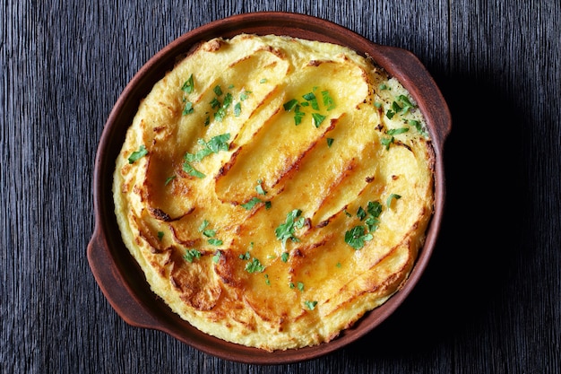 Baked mashed potatoes with parmesan cheese and butter in a baking dish on dark wooden table, horizontal view from above, flat lay, close-up