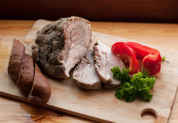 Baked meat on a board with bread, pepper and parsley