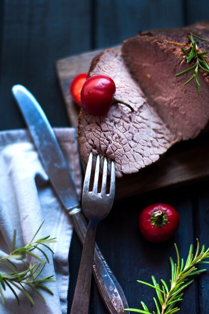 Baked meat with rosemary and red pepper. steak. beef. dinner for men. dark photo. Black background. wooden board.